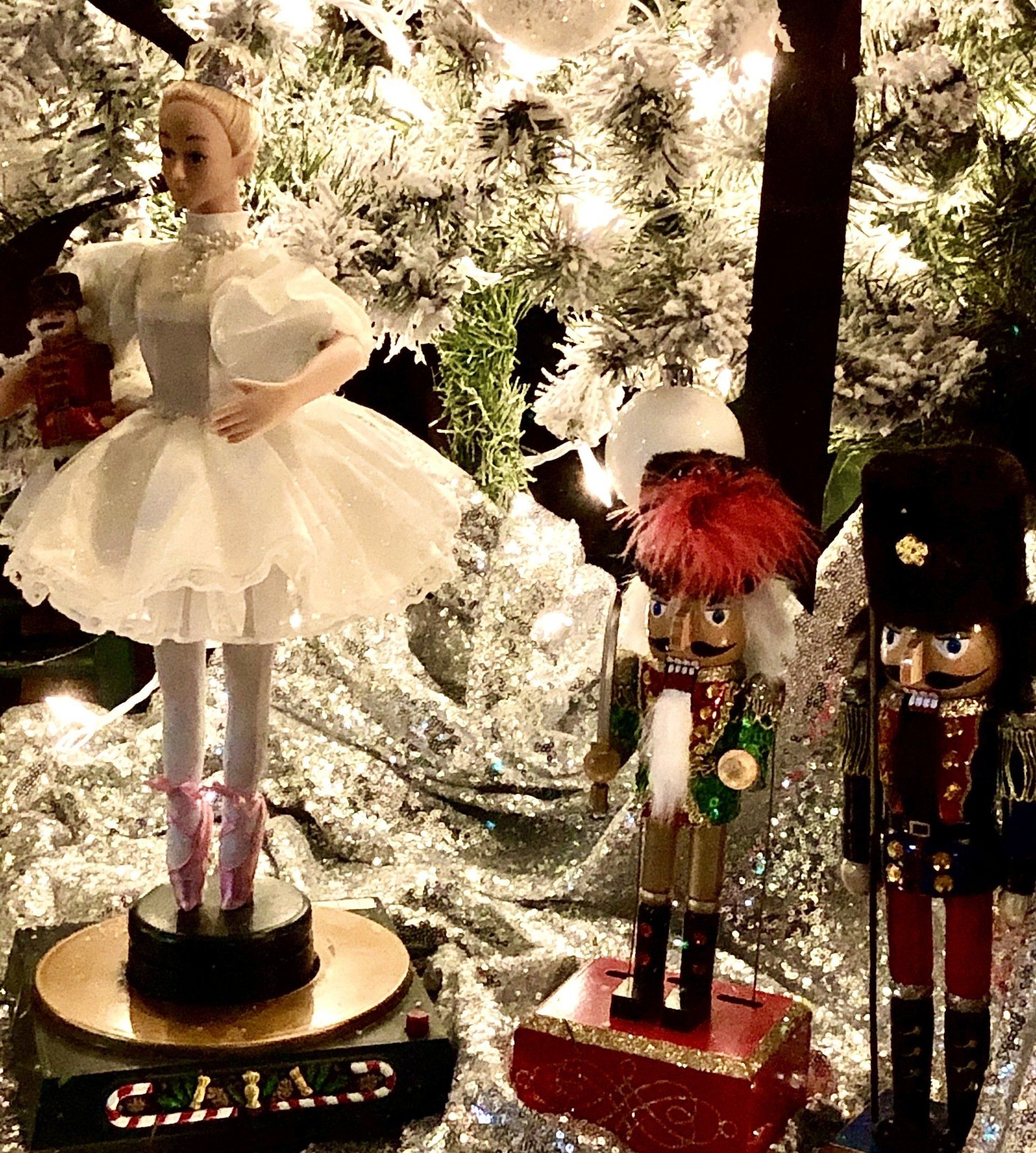 A ballerina and two nutcrackers are sitting under a christmas tree.