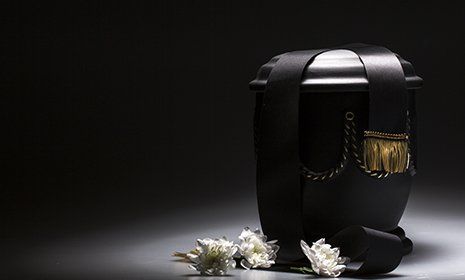 Urna in colore nero con dettagli dorato e fiori bianche al lato