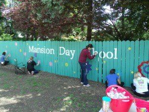 People are painting a blue fence that says mansion day school