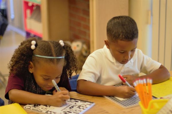 A boy and a girl are sitting at a table writing on a piece of paper.