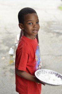 A young boy in a red shirt is holding a plate of food.