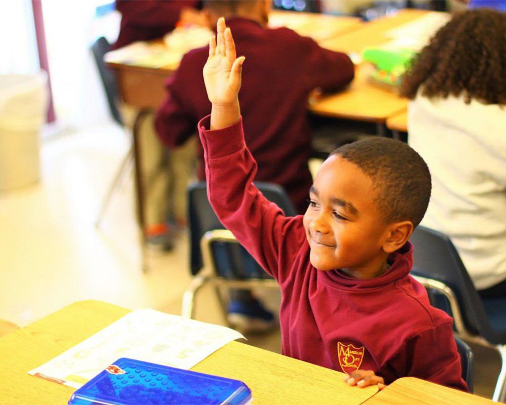 A young boy is raising his hand in a classroom to answer a question