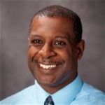 A man in a blue shirt and tie is smiling for the camera.