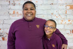 Two young boys are posing for a picture in front of a brick wall.
