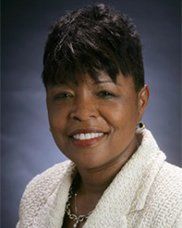 A woman in a white jacket and necklace is smiling for the camera.
