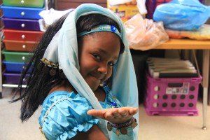 A little girl is wearing a blue dress and a head scarf