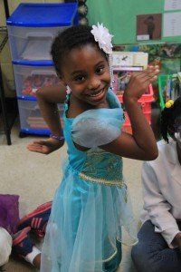 A little girl is wearing a blue dress and a flower in her hair.