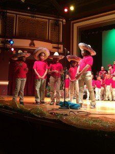A group of children wearing sombrero hats are singing into microphones on a stage.
