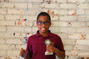 A young boy is holding a trophy in front of a brick wall.
