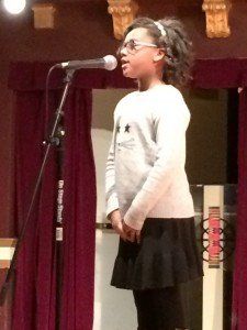 A young girl is singing into a microphone on a stage