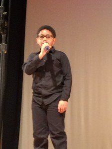 A young boy is singing into a microphone on a stage.