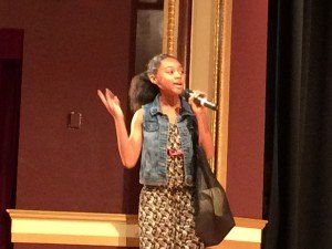 A young girl is singing into a microphone on a stage.