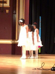 Three little girls in white dresses are standing on a stage