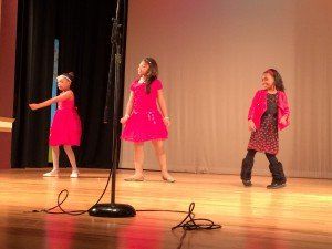 Three young girls are dancing on a stage in front of a microphone.