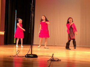 Three young girls are singing into microphones on a stage.