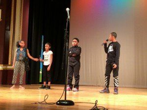 A group of children are singing into microphones on a stage.