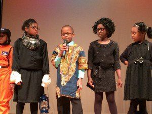 A group of children are standing on a stage and one of them is holding a microphone