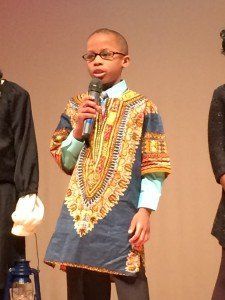 A young boy is holding a microphone and wearing glasses