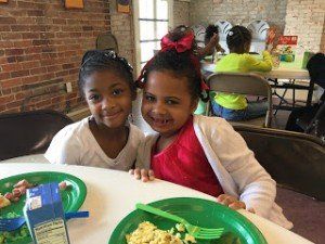 Two little girls are sitting at a table with plates of food.