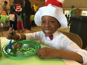 A young boy in a cat in the hat costume is sitting at a table with a plate of food.