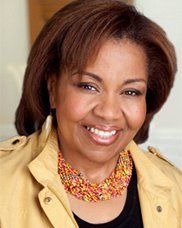 A woman wearing a yellow jacket and a necklace is smiling for the camera.