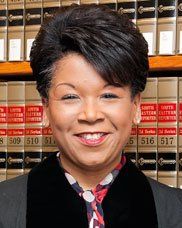 A woman is smiling in front of a bookshelf filled with books.