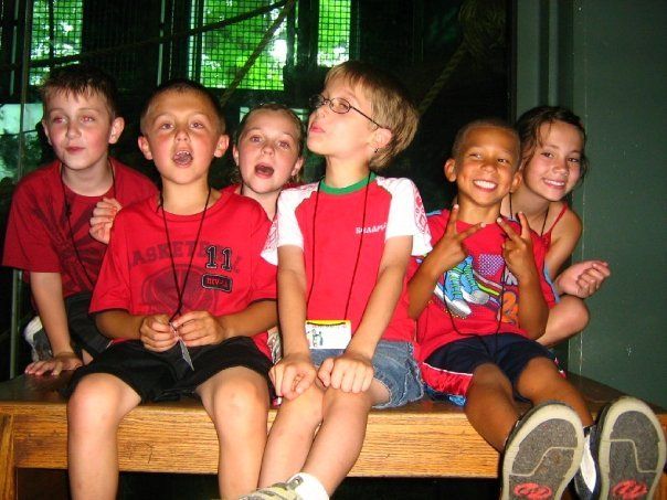 A group of children are sitting on a bench and one of them is wearing a red shirt that says abercrombie