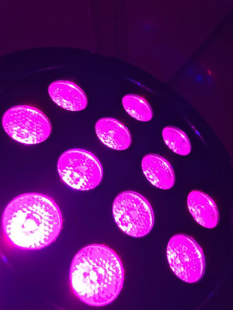 Een close-up, schuin genomen opname van een ronde podiumlamp met meerdere LED's die een levendig paars licht uitstralen.