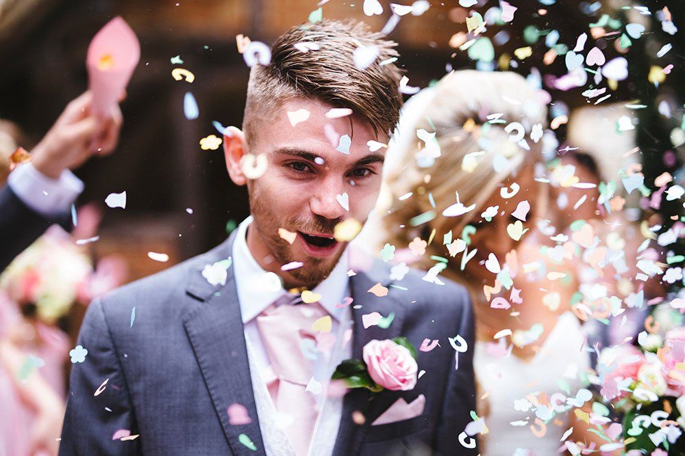 Een gelukkig paar op hun bruiloft, omringd door kleurrijke, neervallende confetti.