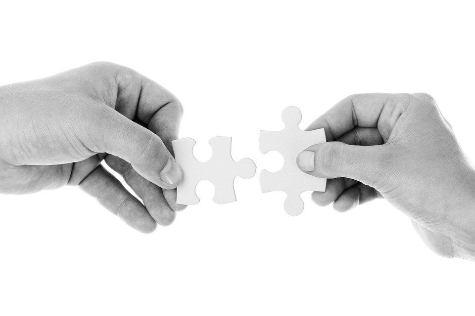 Two hands piecing together pieces of a jigsaw puzzle.