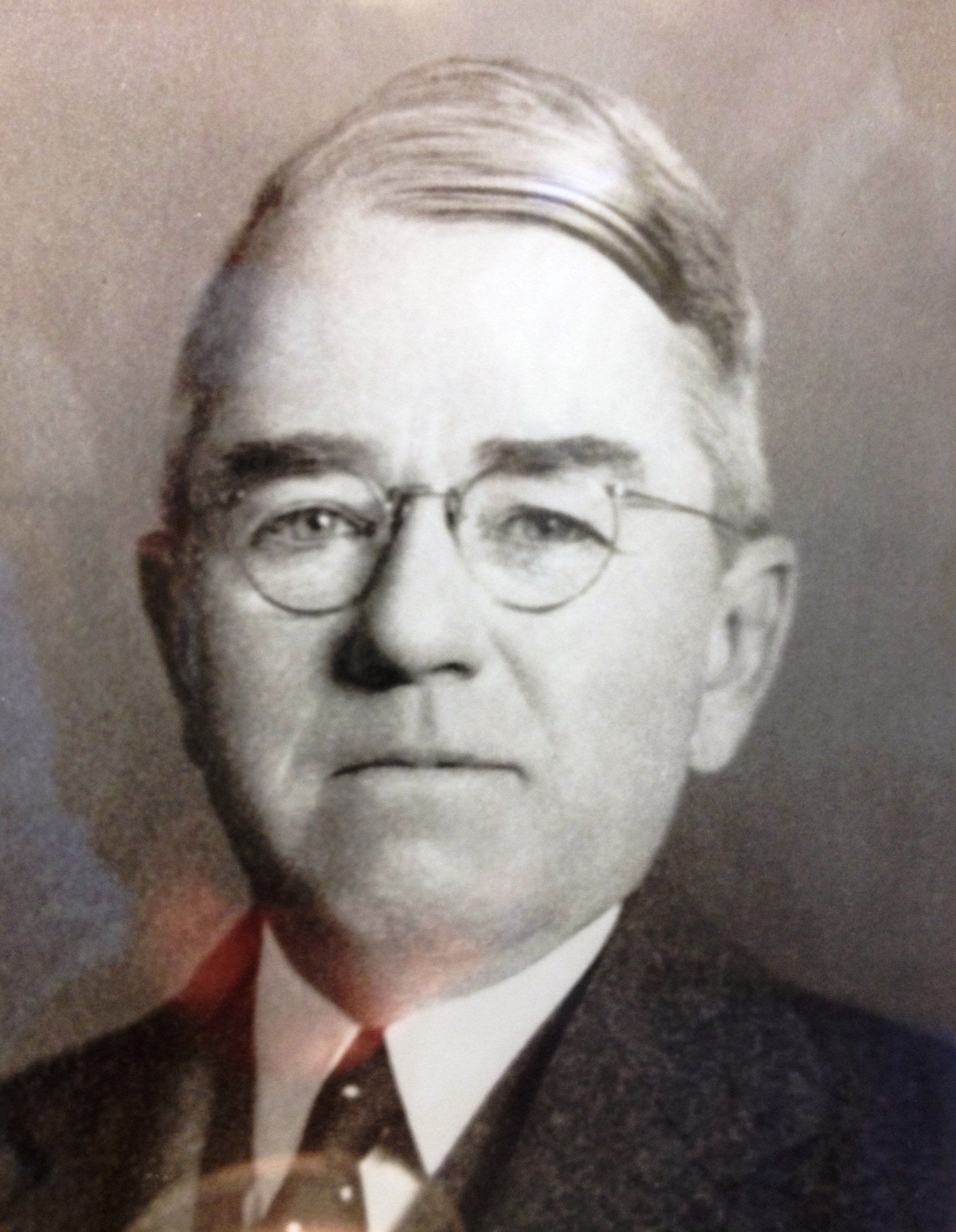 A black and white photo of a man wearing glasses and a suit
