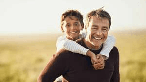 A man is giving a boy a piggyback ride in a field.