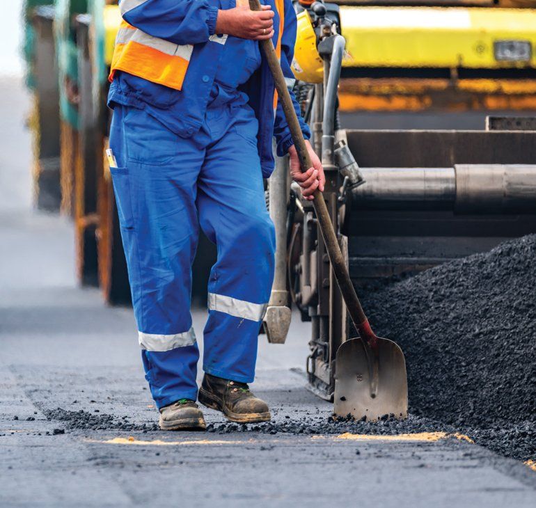 Asphalt Parking Lots — Worker Holding A Shovel With Paving Machine In Kent, WA