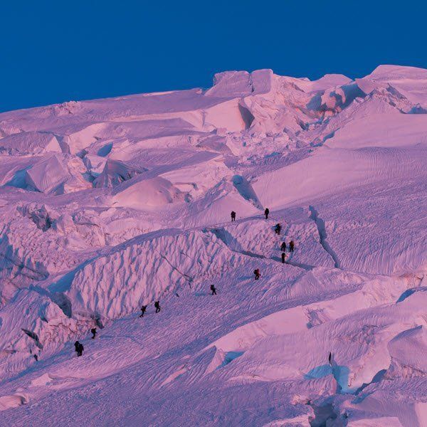 People climbing a snow-covered mountain at dusk. Purple and white hues.