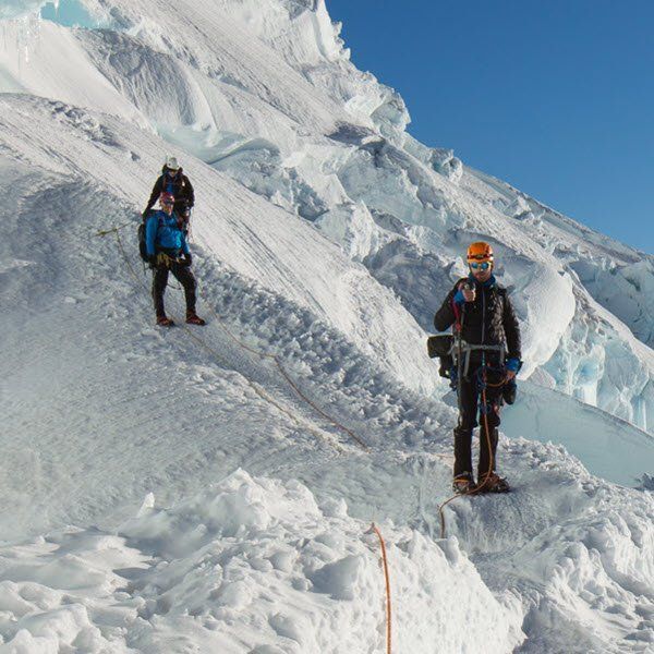 Mountain climbers ascend a snowy glacier, roped together. Blue sky, bright sunlight.