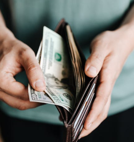 Hands opening a brown wallet with U.S. dollar bills inside