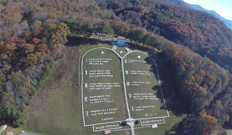 Aerial view of a large heart-shaped memorial lawn with white text, surrounded by autumn trees.