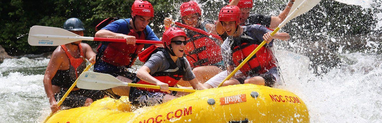 Whitewater rafters in red helmets paddling a yellow raft through splashing rapids