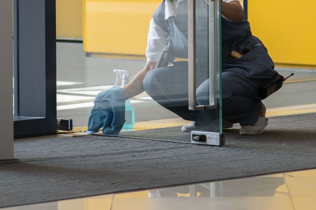 Pulizia professionale di una porta vetrata all'interno di un edificio commerciale