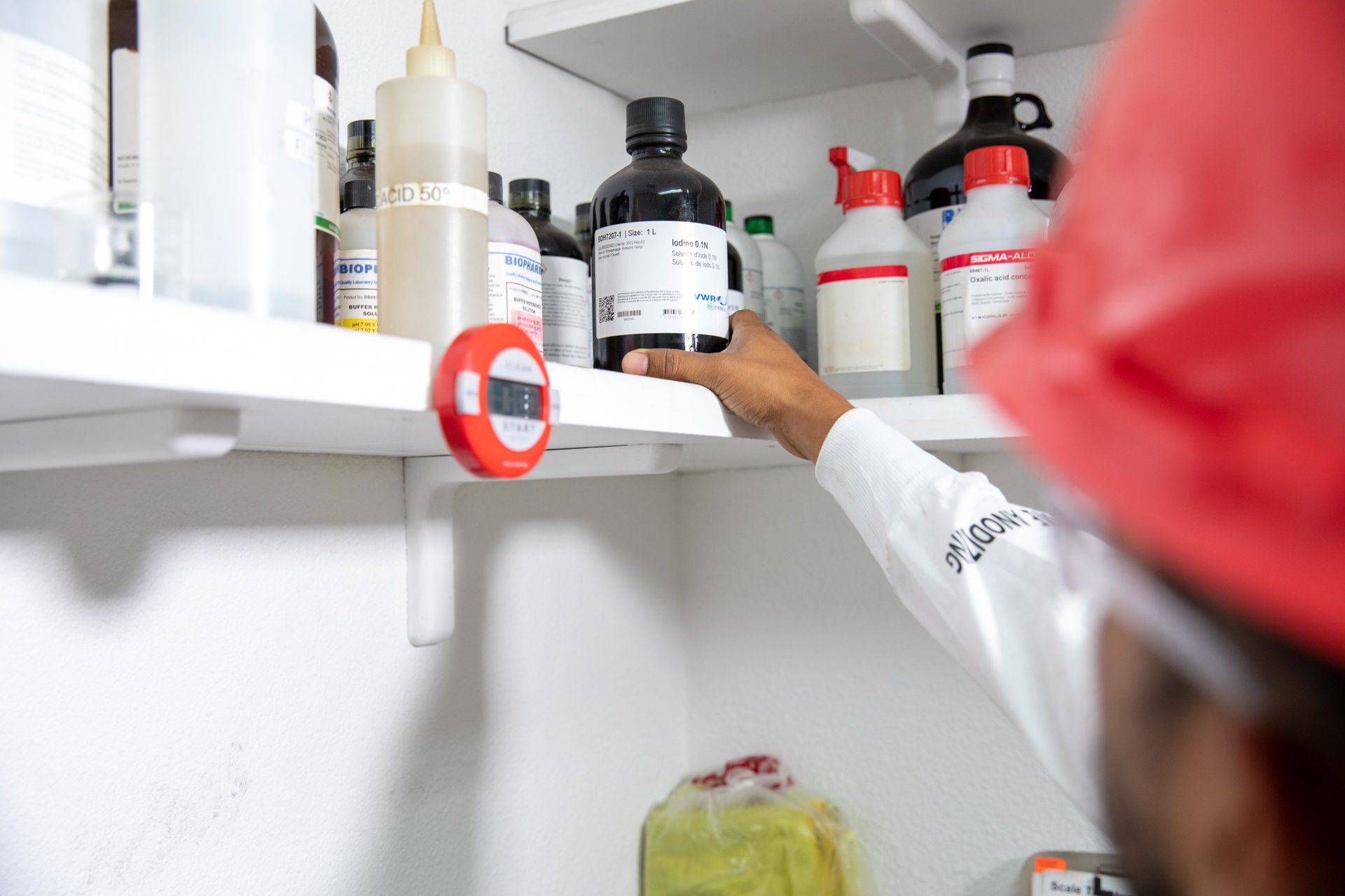 Man in lab coat reaches for chemicals on shelf