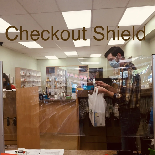 A man wearing a mask is standing in front of a checkout shield in a store.