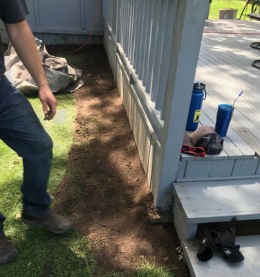 Person standing near a dirt patch along a deck's side. Brown soil and deck with blue bottles and hat.