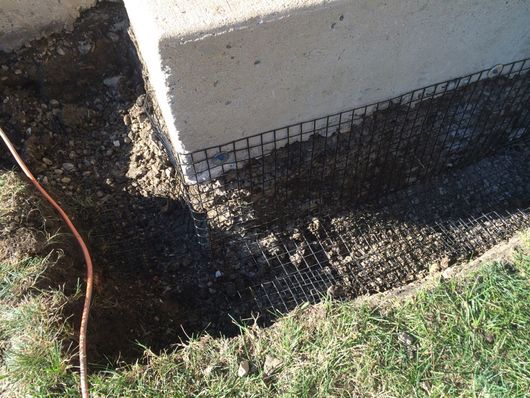 Exposed foundation edge with wire mesh against dirt and grass.