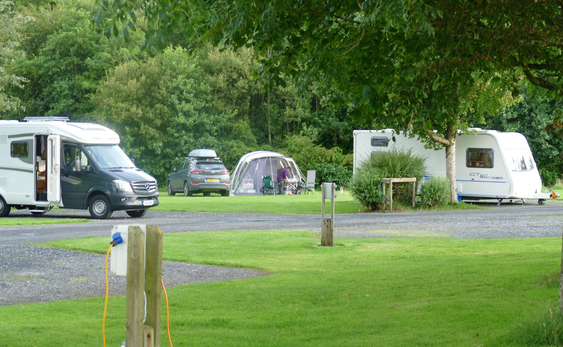 A motorhome is parked in a grassy field next to a tent.