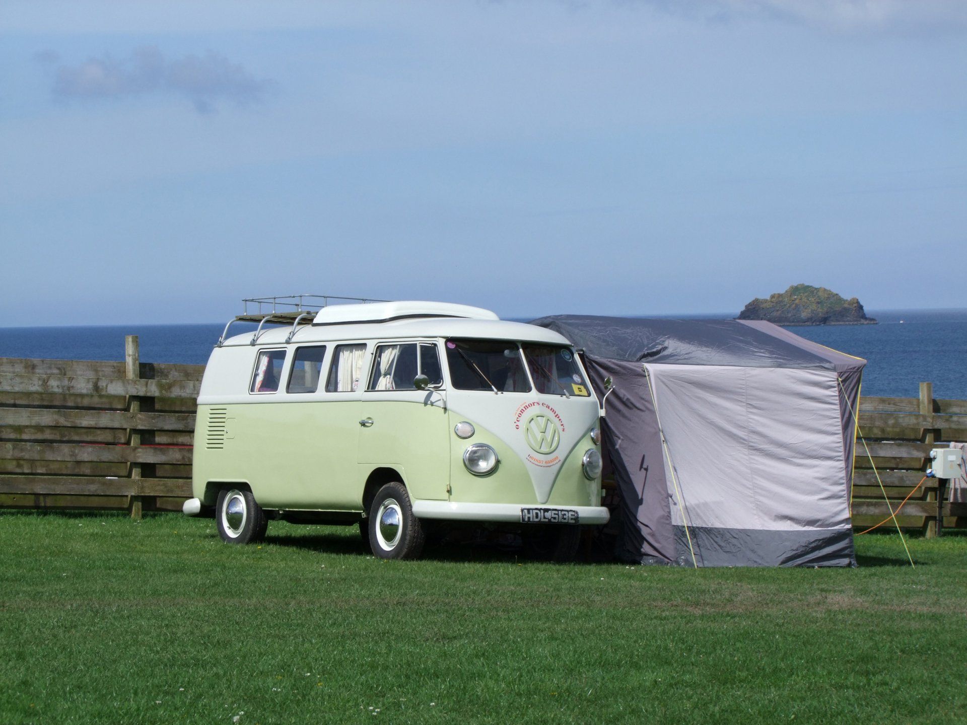 A green camper van is parked in a grassy field next to a tent.