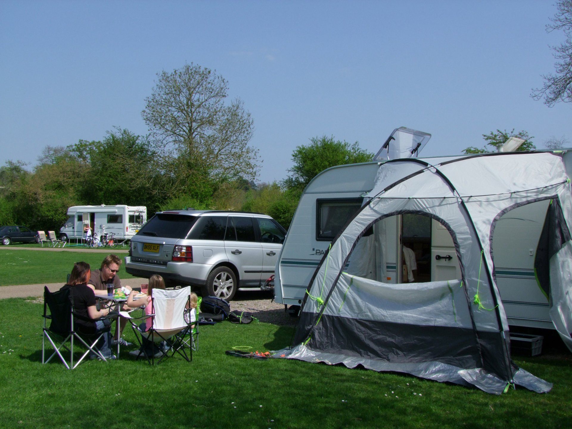 A group of people are sitting at a table in front of a caravan.