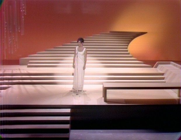 Scene from Barbra's TV show in which she stand in front of a disappearing staircase in an off white gown.