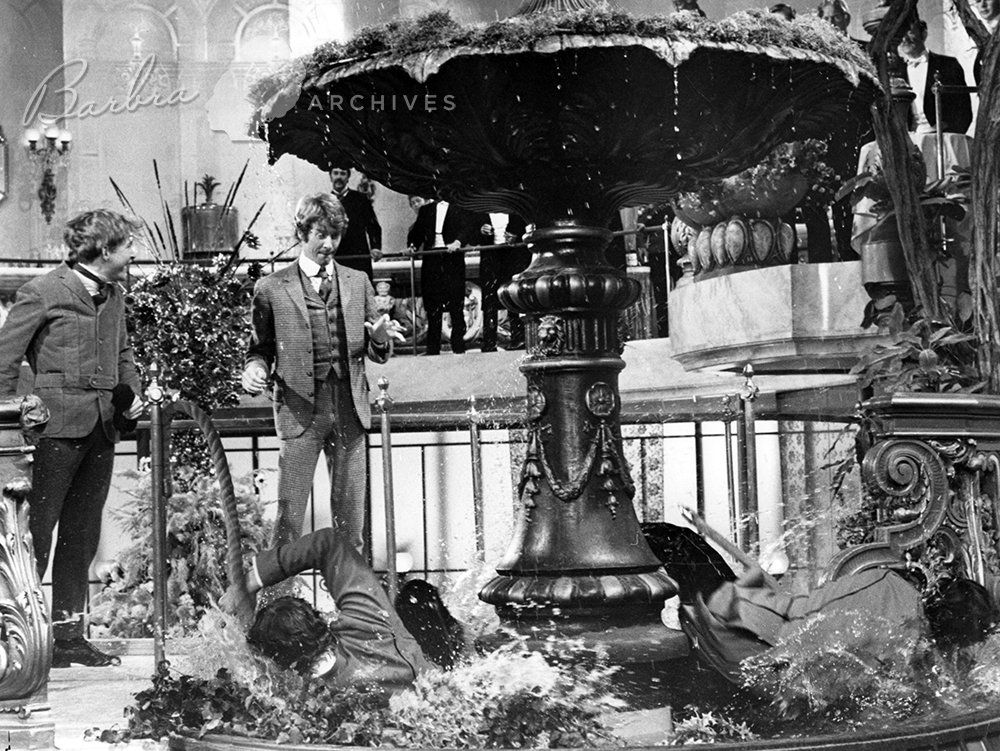 Barnaby and Cornelius watch two men in the fountain