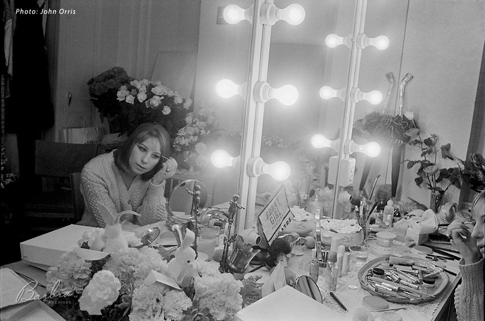 Streisand applies makeup in mirror.