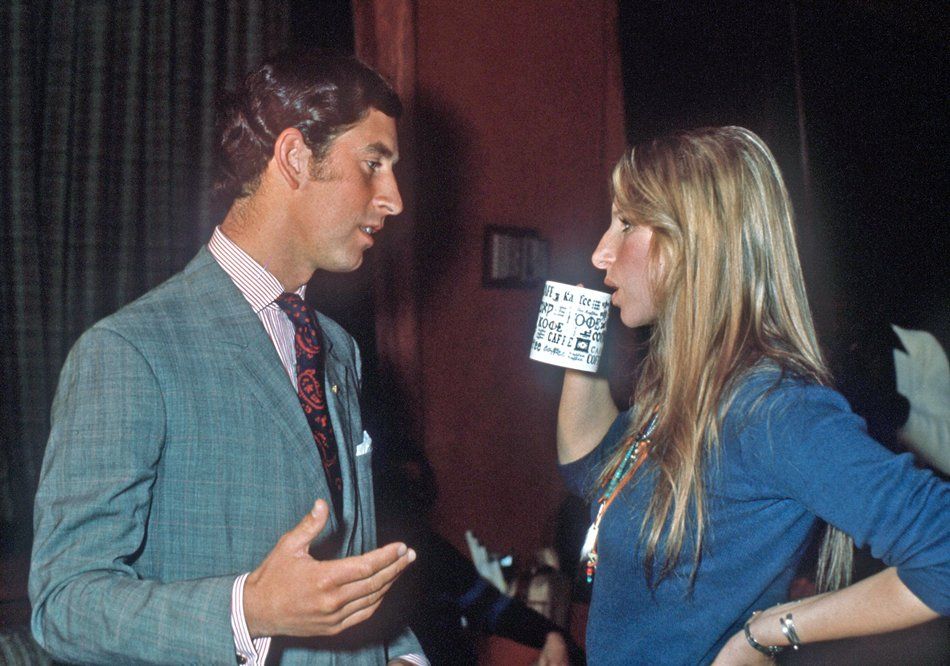 Prince Charles and Streisand  talking indoors, facing each other as Barbra drinks out of a coffee cup.